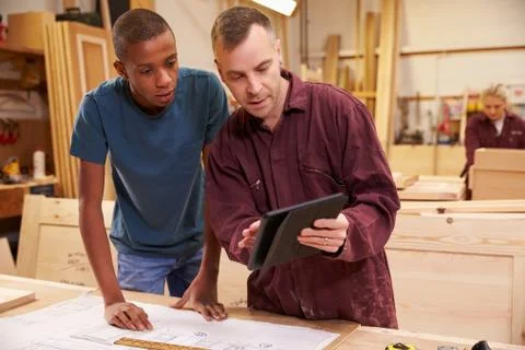 Carpenter With Apprentice Looking At Plans In Workshop Stock Photos