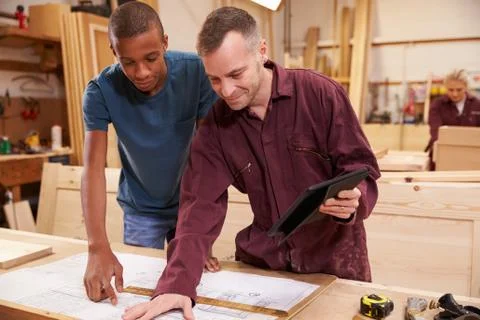 Carpenter With Apprentice Looking At Plans In Workshop Stock Photos