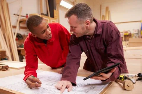 Carpenter With Apprentice Looking At Plans In Workshop Stock Photos