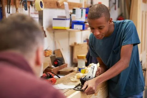 Carpenter With Apprentice Planing Wood In Workshop Foto stock