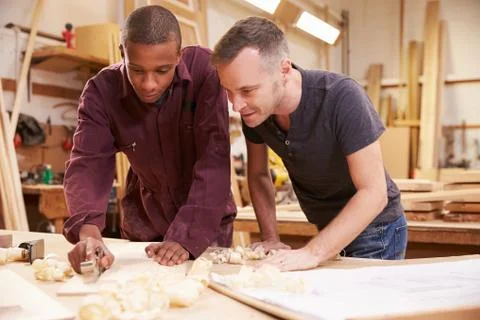 Carpenter With Apprentice Planing Wood In Workshop 스톡 사진