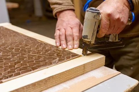 Carpenter assembles boards on the door frame with pneumatic stapler Stock Photos