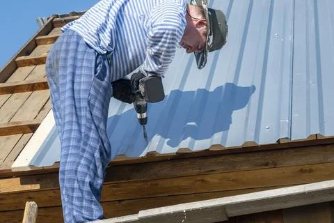 Carpenter, builder fixes screws in galvanized sheets on the roof of the house Stock Photos