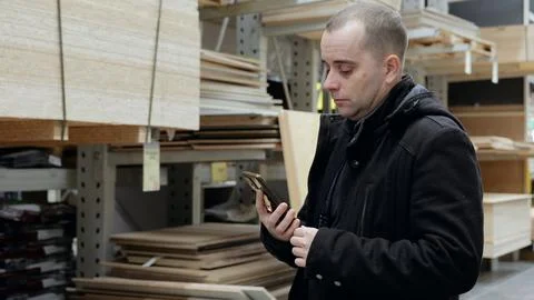 Carpenter checking wood material on smartphone inside warehouse, scrolling Stock Photos