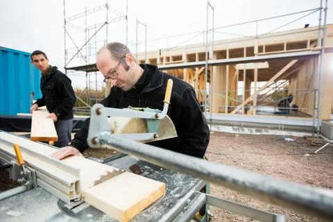 Carpenter Cutting Wood Using Table Saw While Colleague Assisting Foto stock