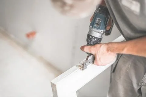 A carpenter disassembles the fittings from a window frame using a screwdriver Stock Photos