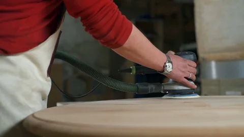 Carpenter gradually polishing a round plank with an electric sander in workshop Stock Footage 74492426