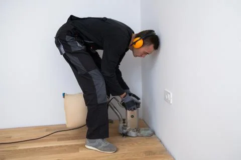 Carpenter grinder parquet in a narrow corner with a small machine Stock Photos