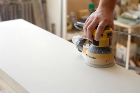 Carpenter grinds the surface of the facade before assembling furniture on a b Stock Photos