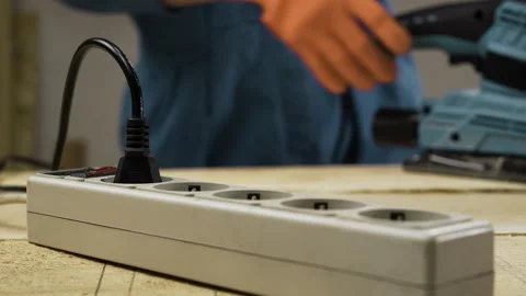 Carpenter hands plugging electric cord into power strip for sanding machine Stock Footage 329111478