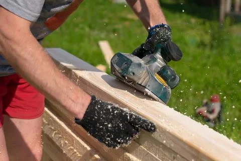 Carpenter hands use an electric tool to process raw lumber Stock Photos