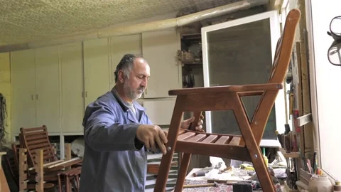 A carpenter in his workshop assembles a handmade chair, screws a bolt, secures Stock Footage 219961987