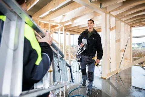 Carpenter Holding Drill Machine While Looking At Colleague Carry Stock Photos