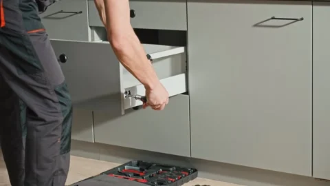 Carpenter installing and adjusting drawer front in modern kitchen cabinet Stock Footage 306577748