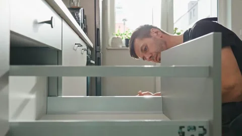 Carpenter installing and adjusting drawer front in modern kitchen cabinet Stock Footage 307830457