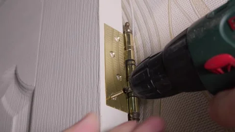 Carpenter installing golden hinge on white door with electric screwdriver Stock Footage 304118003