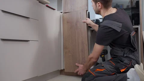 Carpenter installing kitchen cabinet door panel during furniture assembly Stock Footage 329480838