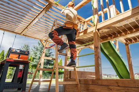 Carpenter on a ladder assembling a wooden backyard playset Foto stock