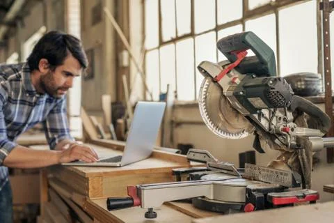 Carpenter leaning on a workbench full of tools working online Stock Photos