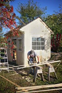 Carpenter Man Using Circular Saw Building a Small Garden Cottage Shed Stock Photos