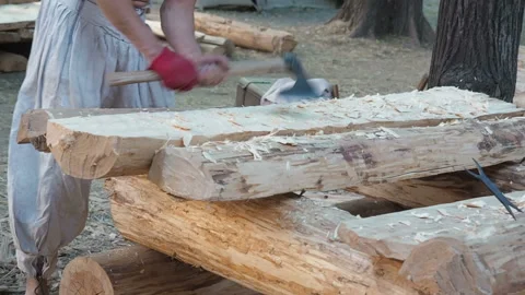 Carpenter in medieval cotton clothes working with hardwood with an ax. A man Stock Footage 119285433