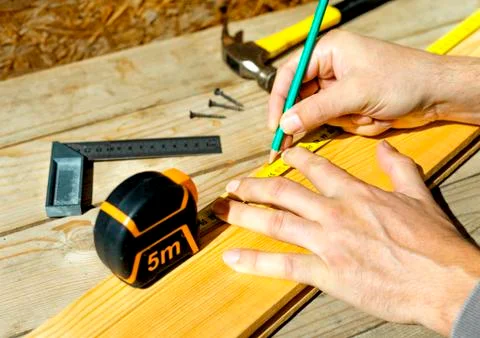 Carpenter notes with pencil using measuring tape on the board, marks for saw Stock Photos