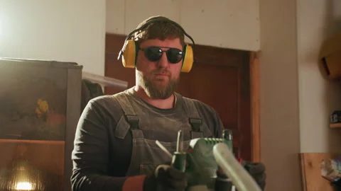 Carpenter Operates Power Tool in Workshop with Protective Gear featuring Vídeo Stock 347106468