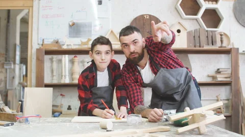 Carpenter pointing at something and little son looks at it at workshop Stock Footage 102510550