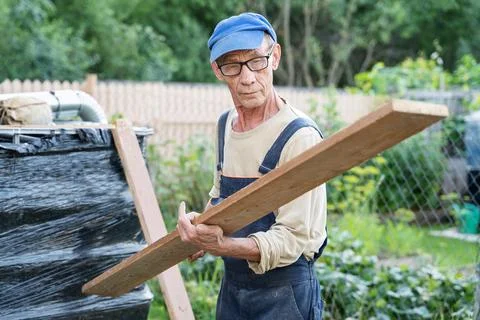 A carpenter processes wooden planks while on the street on a country plot usi Stock Photos
