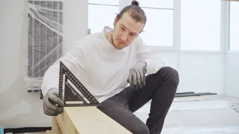 Carpenter in protective gloves makes measurements using a triangle on wood Stock Footage 186789179