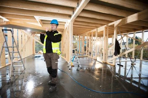 Carpenter In Protective Jacket Carrying Plank On Shoulder At Sit Stock Photos