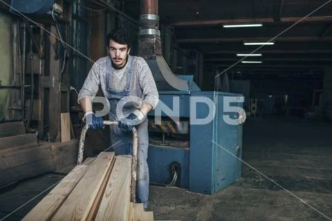 Carpenter pushing stack of wood planks on cart at workshop Stock Photos