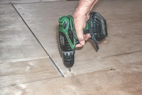 Carpenter screw screwdriver spin into a sheet of plywood. Repair floor Stock Photos