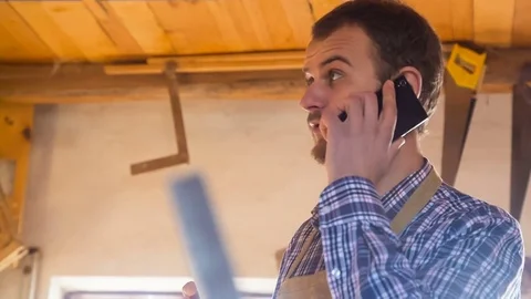 The carpenter speaks by telephone in the workshop on the background of the Stockbeeldmateriaal 84636773