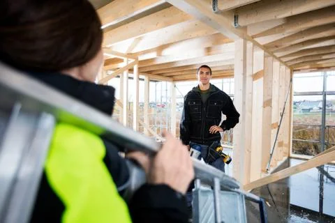 Carpenter Standing While Colleague Carrying Ladder In Incomplete 写真素材