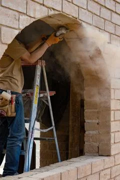 A carpenter on a step ladder grinding an adobe brick frame to accommodate a w Stock Photos