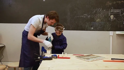 Carpenter teaches the boy to work with an electric jigsaw  on wood Stock Footage 102240379