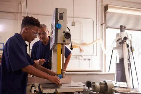 Carpenter Training Male Apprentice To Use Mechanized Saw 库存照片