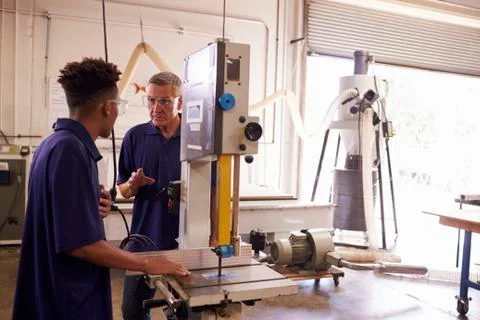 Carpenter Training Male Apprentice To Use Mechanized Saw Stock Photos