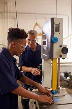 Carpenter Training Male Apprentice To Use Mechanized Saw Stock Photos