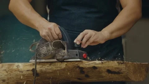 Carpenter uses an electric hand planer to flatten the surface of a wooden log Stock Footage 266866600