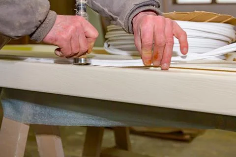 Carpenter uses hand tool to placed rubber tape on the wooden door frame. Stock Photos