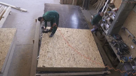 Carpenter uses nail gun to fix board on wooden construction in factory hall. Stock Footage 98443087