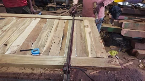 Carpenter using a clamp on wooden planks in a workshop with tools scattered.. Video stock 266864173