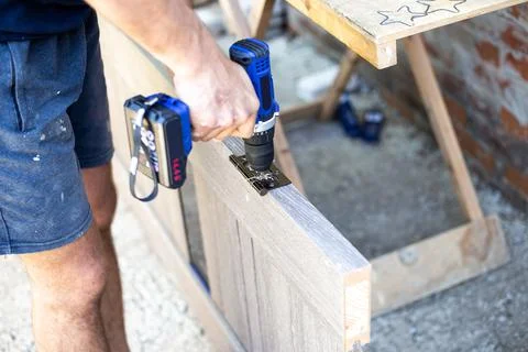 A carpenter is using an electric drill to screw the hinge hardware onto a woo Foto stock