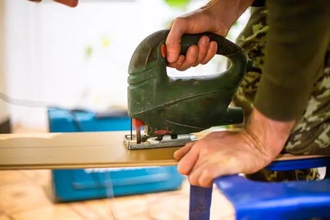 Carpenter using an electric jigsaw to create a piece of art. The carpenter is Stock Photos