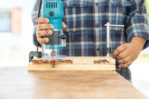 The carpenter using a electric trimmer to cut edging wooden board. Stock Photos