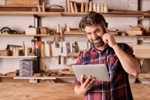 Carpenter using a mobile phone and holding digital tablet Foto stock