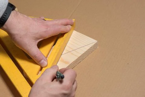 Carpenter using a pencil and old square marking a diagonal line on a wood board Stock Photos