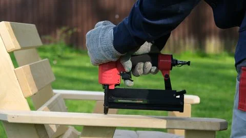 Carpenter using a red pneumatic nail gun to assemble a wooden deck chair armr Stock Photos